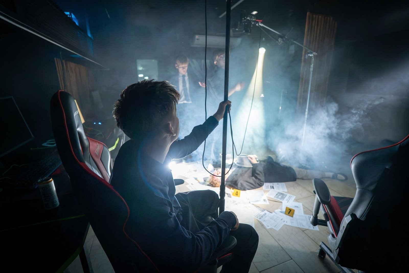 A crew member in a chair holds a pole over the set as a spotlight beam cuts through the haze.