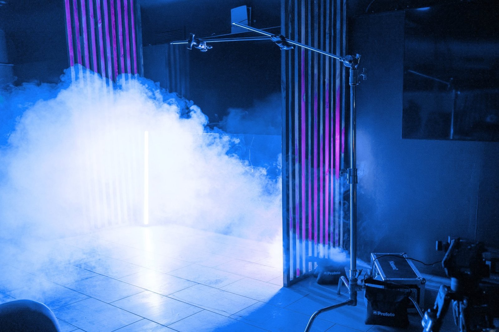 Haze rolls across a set lit blue, with a light on a boom stand and a smoke machine on the floor.