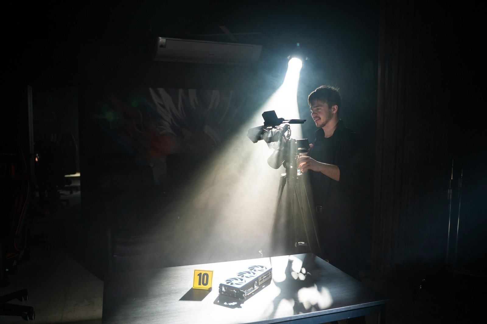 A camera operator holds a rigged camera in the beam of a spotlight over a table of props.