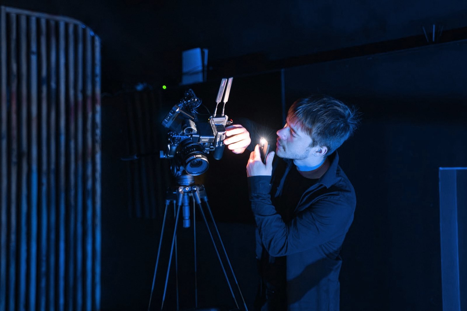 A camera operator checks focus on a camera on a tripod in the dark.