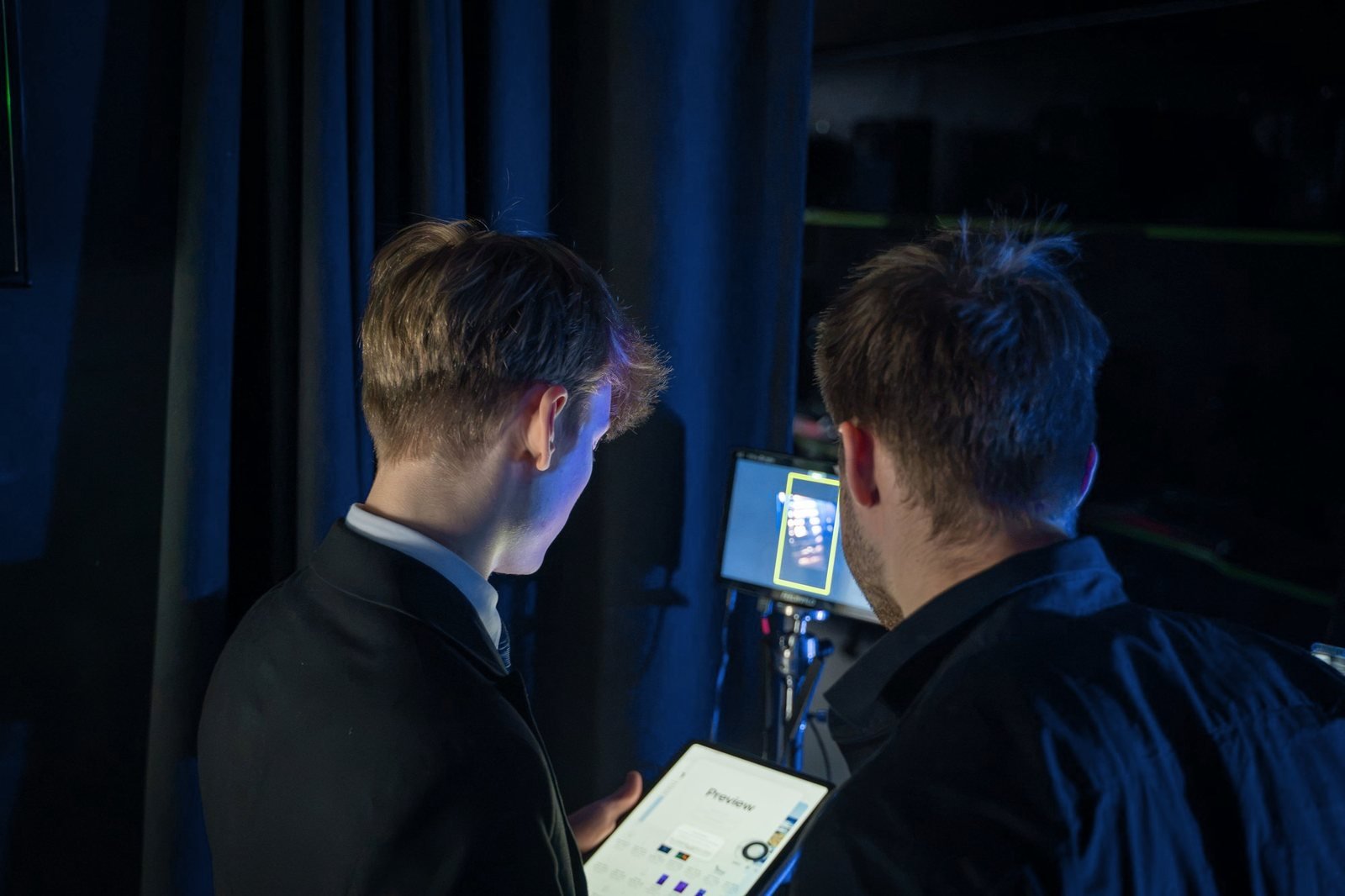 Simonas reviews a tablet with a crew member beside a monitor.