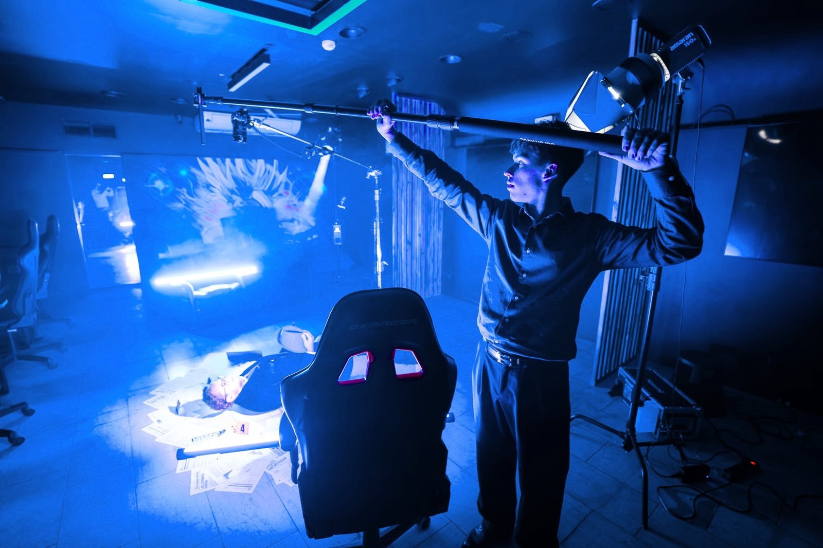 A boom operator holds a microphone over a scene in blue light.