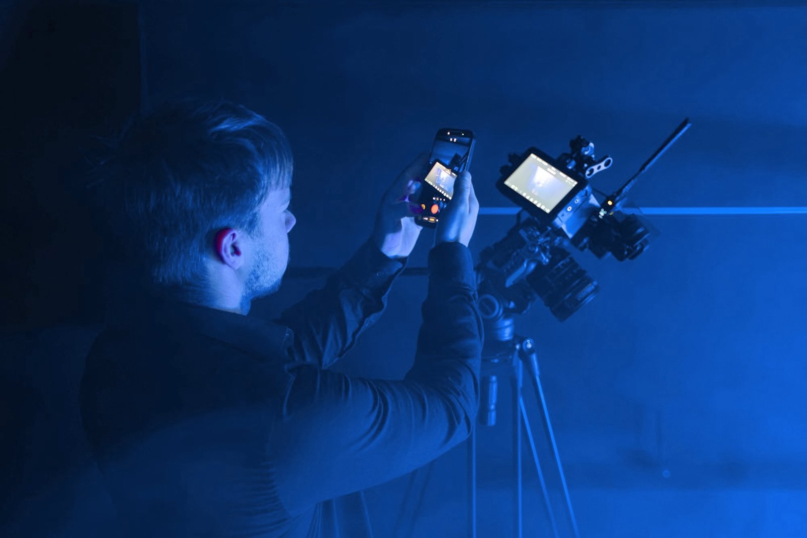 A camera operator adjusts a rig with a monitor in blue light.