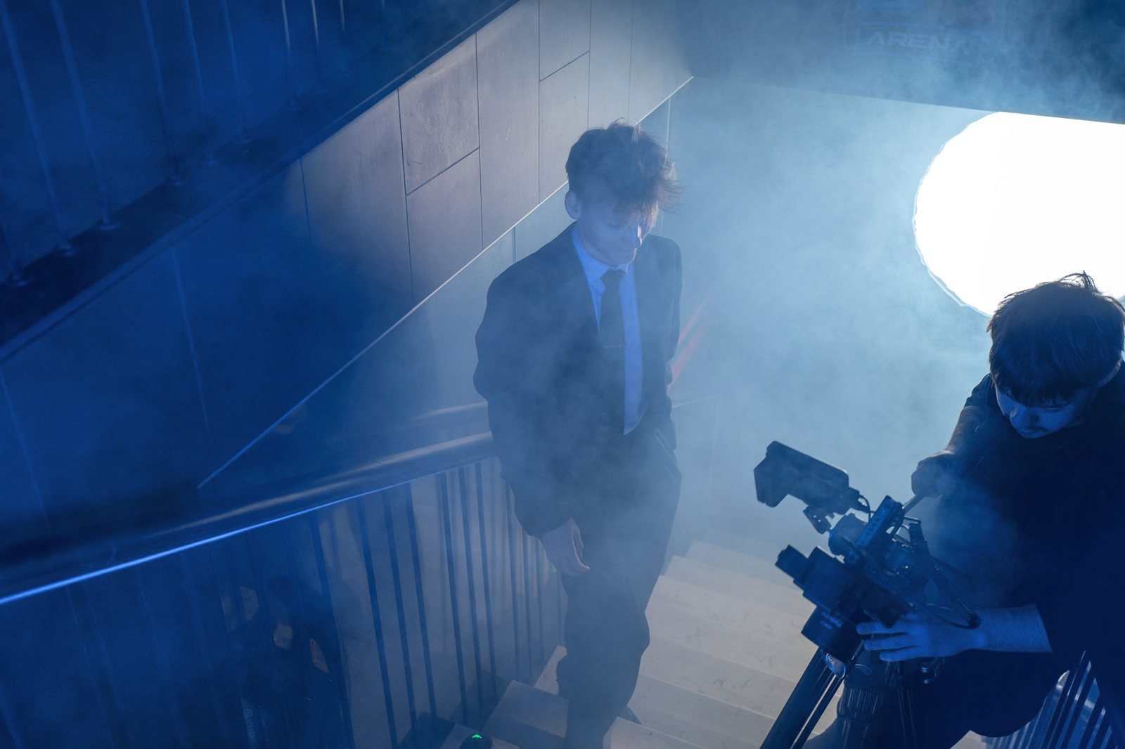 A camera operator films Simonas on smoky stairs.