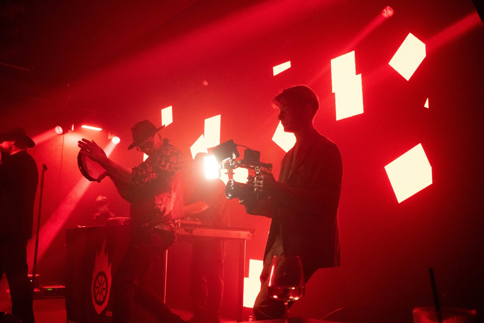 Videographer with a gimbal filming a performer under dramatic red stage lighting